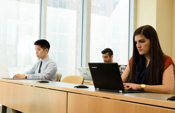Three Students Pictured at Classroom Desks with Laptops