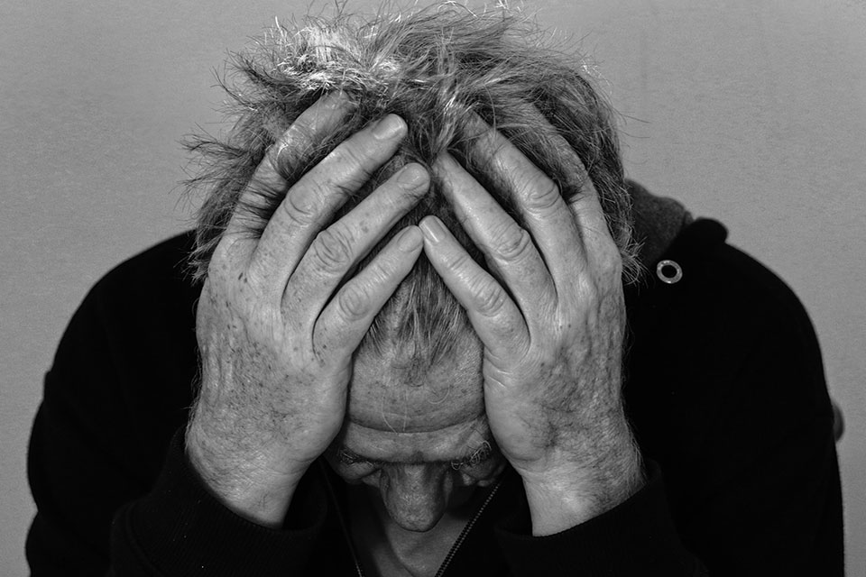Black and white photograph of an older man clutching his head in distress.