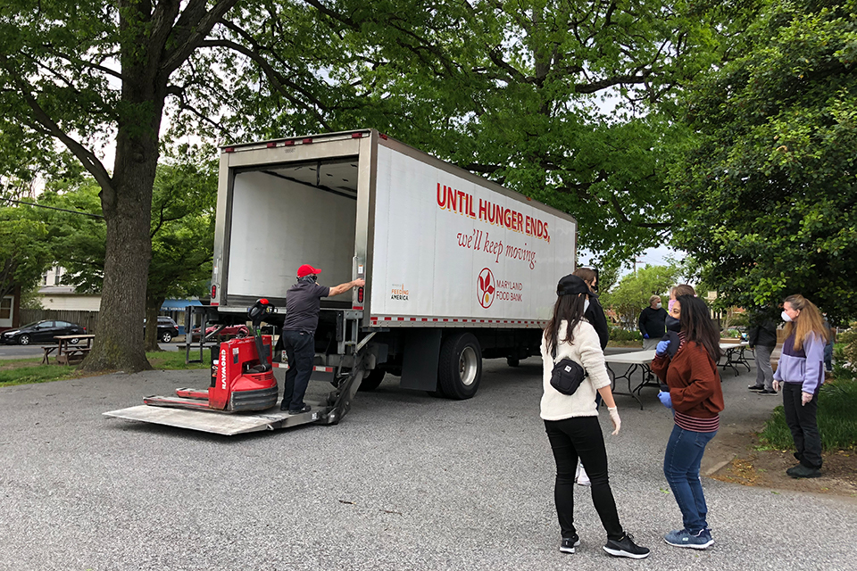 Students wait alongside delivery truck as food is loaded for delivery.