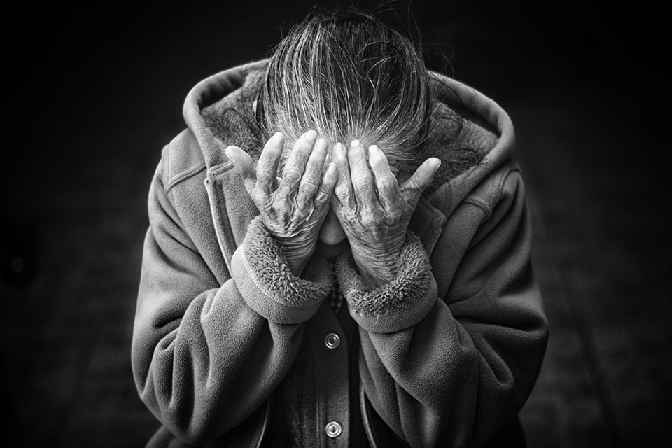 Older adult woman holding her head in her hands.