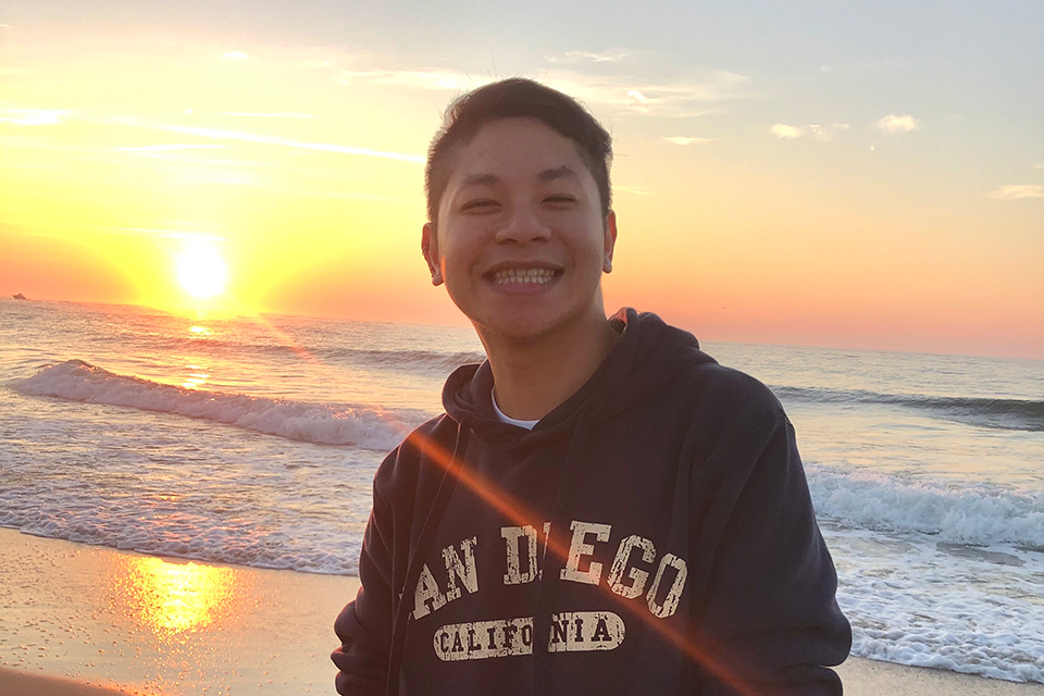 Headshot of Minh Ta smiling in front of sunset and ocean.