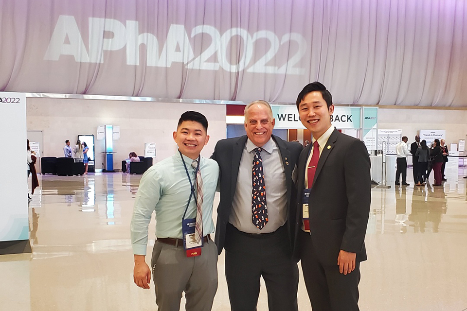 Three people stand in front of an APhA2022 banner.