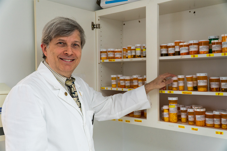 Scott Kuperman reaches into a medicine cabinet filled with pill bottles.